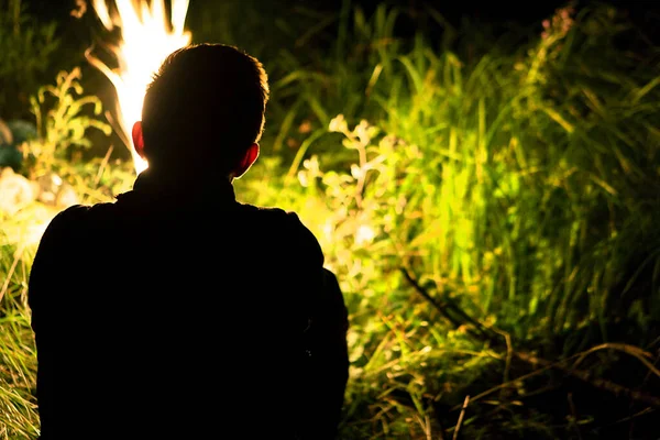 Akşam ateşin yanında dinlenin. Genç bir adam ateşin yanında oturur. Kamp yapmak. Ateş.