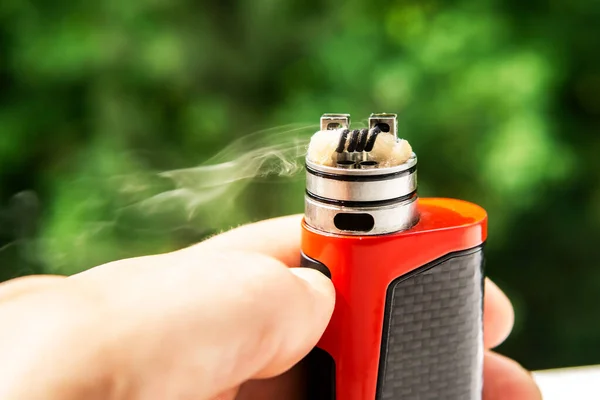 Ağaçların arkasında elektronik sigara, görünür sarmal yün ve buhar. Bobin temizleme.