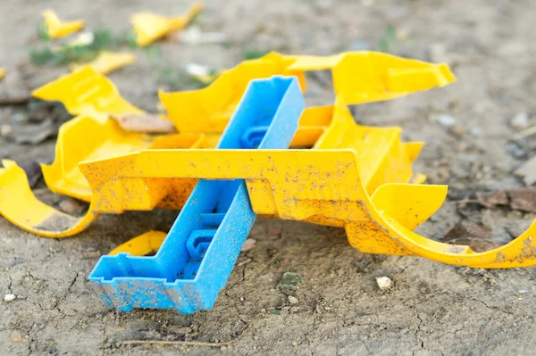 A broken plastic toy lies on the ground. Broken car without wheels