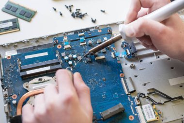 Adamın biri dizüstü bilgisayarı tamir ediyor, beyaz arka planda bir dizüstü bilgisayarı parçalıyor, ana bilgisayarı lehimliyor.