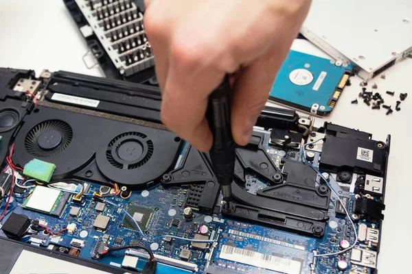 Atölyede dizüstü bilgisayar tamiri, erkek eli tornavida tutuyor.