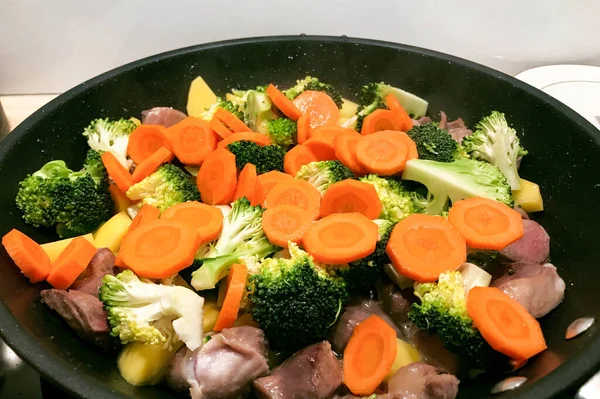 Broccoli with carrots and meat is cooked in a pan