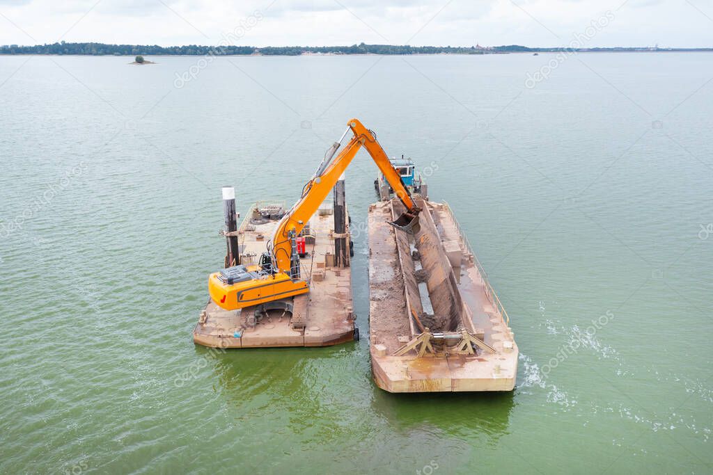 Extraction of sand from the river, excavator digs out sand from the bottom of the lake and unloads it on a floating barge, mining