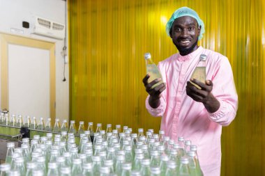 Afrikalı erkek fabrika işçisi içecek fabrikasında yeşil meyve suyu şişesi ya da fesleğen tohumu içeceği tutuyor.