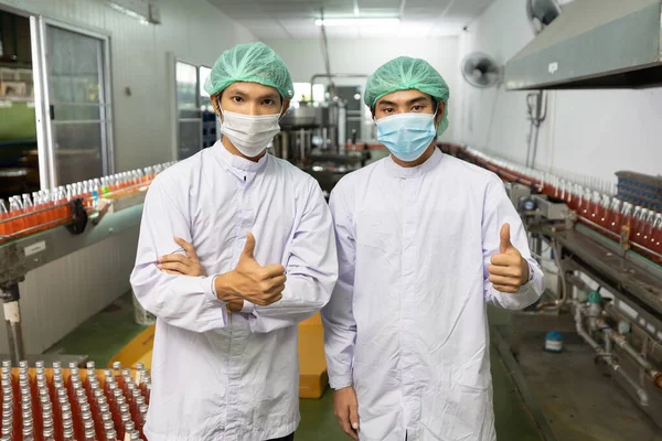 portrait couple of asian male factory worker wearing medical mask and thumbs up post in beverage factory