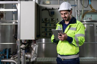 Fabrikada makine kontrol panelinin nasıl kullanılacağını bulmak için tablet bilgisayar kullanan mühendis veya fabrika işçisi