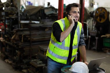 yakışıklı mühendis ya da fabrika işçisi akıllı telefon ve dizüstü bilgisayarı iş hakkında konuşmak için kullanıyor