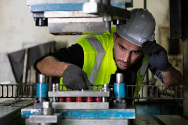 Makine mühendisi koruyucu kask ve eldiven takıyor. Makineyi tamir etmek için anahtar kullanıyor.