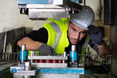 Makine mühendisi koruyucu kask ve eldiven takıyor. Makineyi tamir etmek için anahtar kullanıyor.