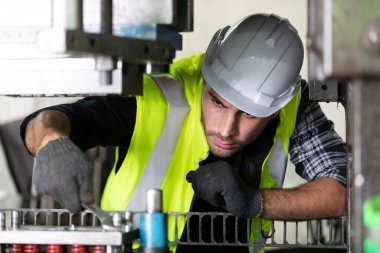 Makine mühendisi koruyucu kask ve eldiven takıyor. Makineyi tamir etmek için anahtar kullanıyor.