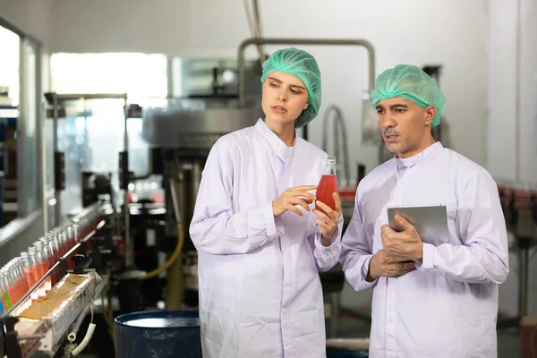two factory workers looking something, talking about project and checking quality of basil seed drink in beverage factory