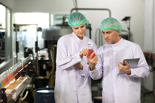 two factory workers talking about project and checking quality of basil seed drink in beverage factory