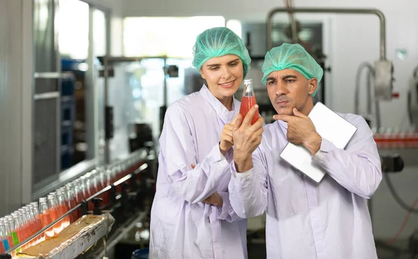 two factory workers talking about project and checking quality of basil seed drink in beverage factory