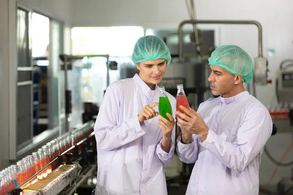 two factory workers talking about project and checking quality of basil seed drink in beverage factory