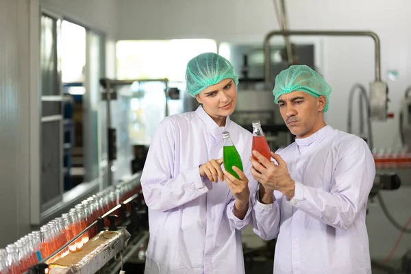 two factory workers talking about project and checking quality of basil seed drink in beverage factory
