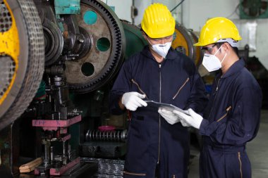 Erkek mühendis ya da fabrika işçisi virüsü korumak için maske takıyor, konuşuyor ve proje hakkında tablet kullanıyor.