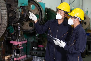 Erkek mühendis ya da fabrika işçisi virüsü korumak için maske takıyor, konuşuyor ve proje hakkında tablet kullanıyor.