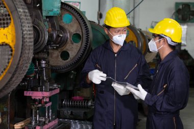 Erkek mühendis ya da fabrika işçisi virüsü korumak için maske takıyor, konuşuyor ve proje hakkında tablet kullanıyor.