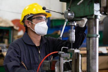 Erkek teknisyen ya da fabrika işçisi virüsü korumak için yüz maskesi takıyor, fabrikadaki makineyi kullanıyor.