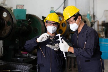Erkek teknisyen ya da fabrika işçisi virüsü korumak için yüz maskesi takıyor, ilkbahara bakıyor ve fabrikada bir metal ölçüyor.
