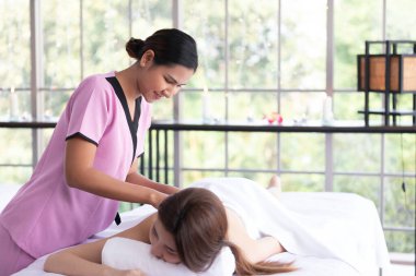 Genç Asyalı masör spa salonundaki kadın müşteriye masaj yaptırıyor.