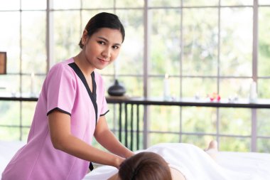 Genç Asyalı masör spa salonundaki kadın müşteriye masaj yapıyor.