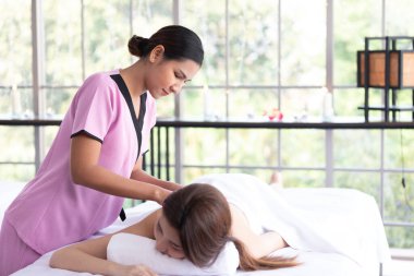 Genç Asyalı masör spa salonundaki kadın müşteriye masaj yaptırıyor.