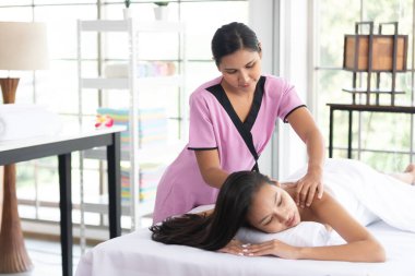 Genç Asyalı masör spa salonundaki kadın müşteriye masaj yaptırıyor.