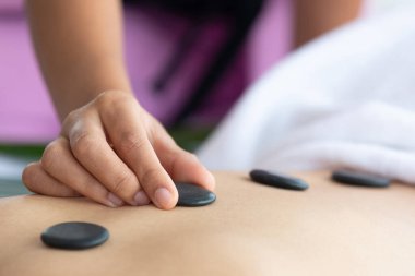 Yakın plan genç Asyalı masör kaplıca salonuna sıcak taş masajı yapıyor.