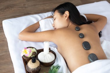 Genç Asyalı bir kadın masaj için kaplıcaya yattı. Yanında bitkisel malzemeler ve spa taşlarıyla.