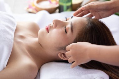 Kapalı gözlerle yatakta yatan ve kaplıca salonunda yüz veya kafa masajı yaptıran genç bir kadın.