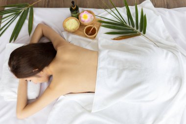 Genç Asyalı bir kadın masaj salonundaki masaj için yatakta uyuyor. Masaj için bitkisel malzemelerle.
