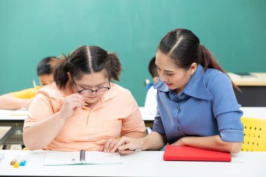 Asyalı engelli çocuk ya da otizm çocuğu sınıfa yardım eden bir kitap ve kadın öğretmen yazıyor
