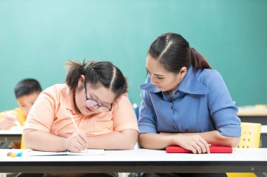 Asyalı engelli çocuk ya da otizm çocuğu sınıfa yardım eden bir kitap ve kadın öğretmen yazıyor