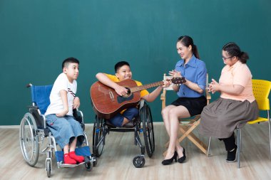 Asya 'lı engelli çocuklar ve kadın öğretmen gitar çalıp eğleniyor. 