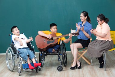 Asya 'lı engelli çocuklar ve kadın öğretmen gitar çalıp eğleniyor.