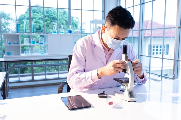 science man wearing medical face mask for protect virus and using microscopes in laboratory