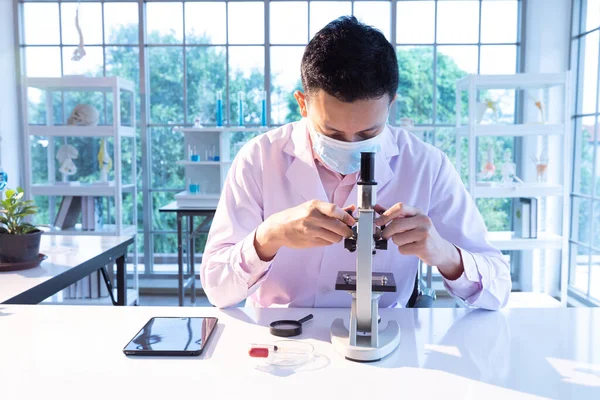 science man wearing medical face mask for protect virus and using microscopes in laboratory