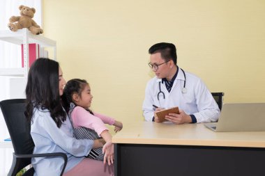 Asyalı doktor konuşuyor ve klinikteki anne ve çocuğa hasta bilgilerini soruyor.