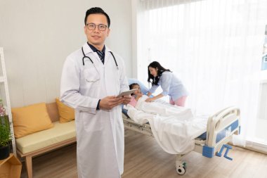 Asyalı doktor elinde tablet tutuyor ve hastaların bilgilerini hastanede buluyor.