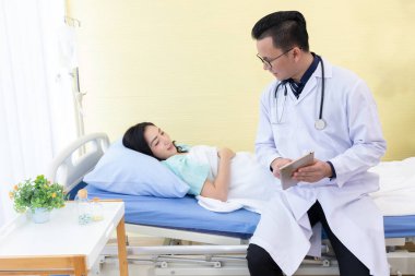 Asyalı doktor hastane odasındaki hasta kadına bir şey anlatıyor.