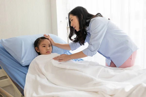 母のサポートで病院のベッドに寝そべっていたアジア系の少女は — ストック写真