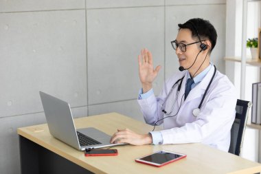 Asyalı doktor laptopa merhaba diyor. Hastanede video konferansı var.