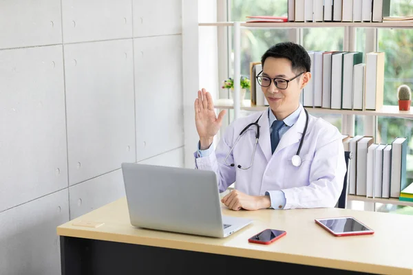 asian doctor say hello with laptop computer having video conference at hospital