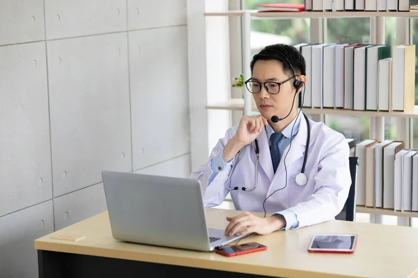 asian doctor talking with patient or co-worker through online video chat with computer in hospital