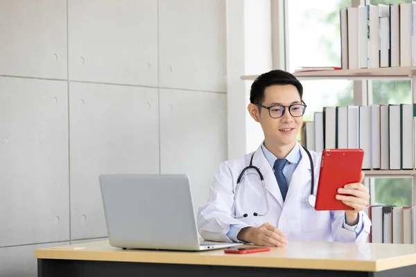 asian doctor talking with patient or his family through online video chat from tablet in hospital