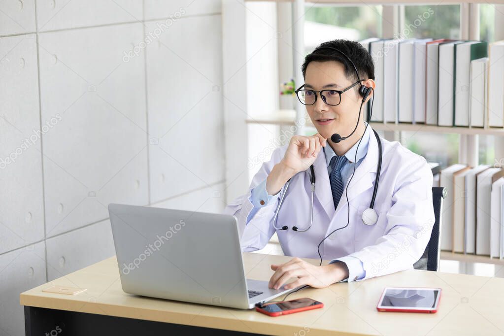 asian doctor talking with patient or co-worker through online video chat with computer in hospital