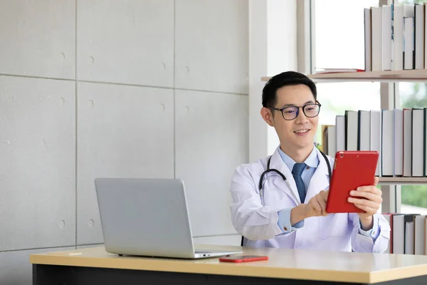 asian doctor talking with patient or his family through online video chat from tablet in hospital