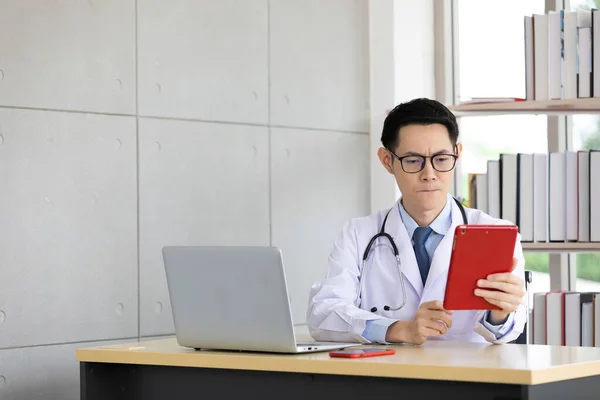 asian doctor talking with patient or his family through online video chat from tablet in hospital