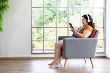 Tombul kadın tablet bilgisayar kullanıyor ve boş zamanlarında müzik dinliyor.